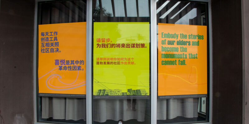 Three posters hanging in a window with text in several languages. 