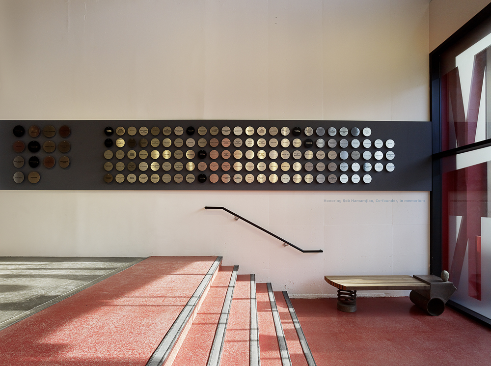 Photo of donor wall metal discs along a grey stripe on the wall with four red steps in front of it.