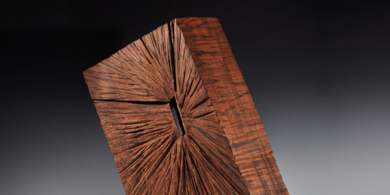 Wood block sculpture with middle cut out slightly and grain lines coming from the middle