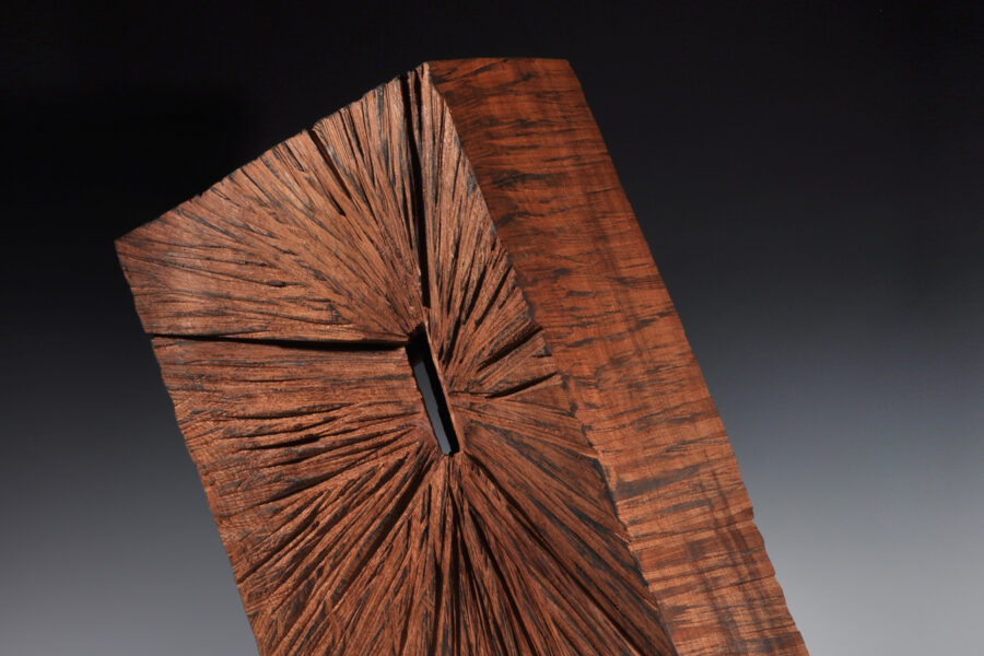 Wood block sculpture with middle cut out slightly and grain lines coming from the middle
