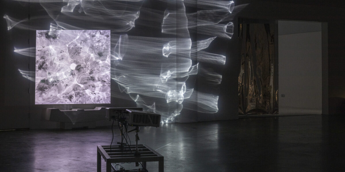 Dark room with a robot that has two projectors on it, projecting abstract lines across the wall