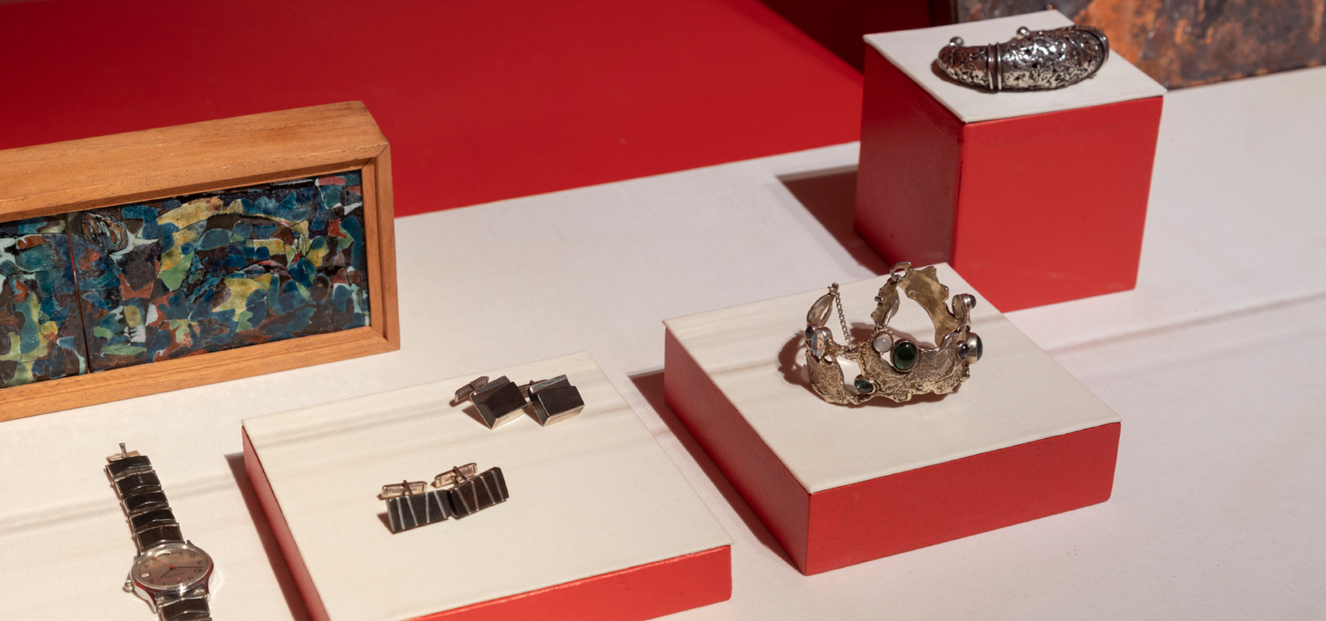 Jewelry on display in gallery with red walls as backdrop