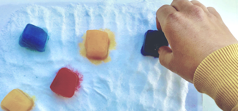 Color ice cubes on and hand reaching out to one white cloth