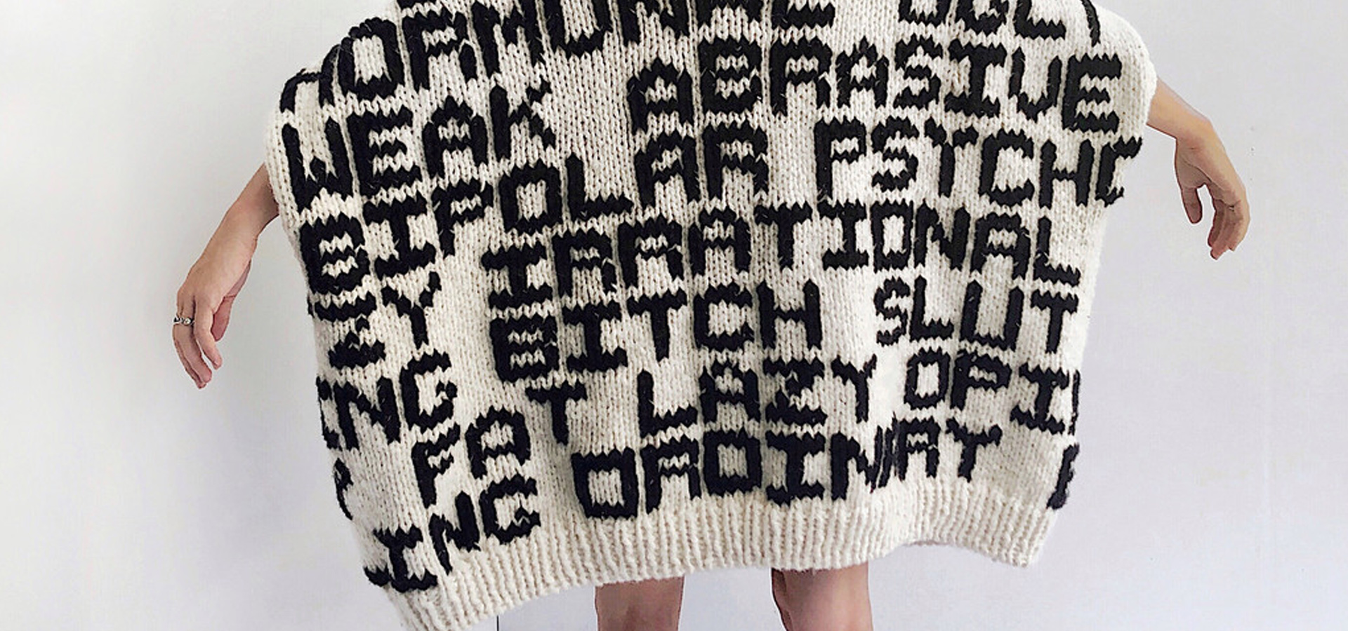 A beige sweater with phrases knitted into it in black yarn.