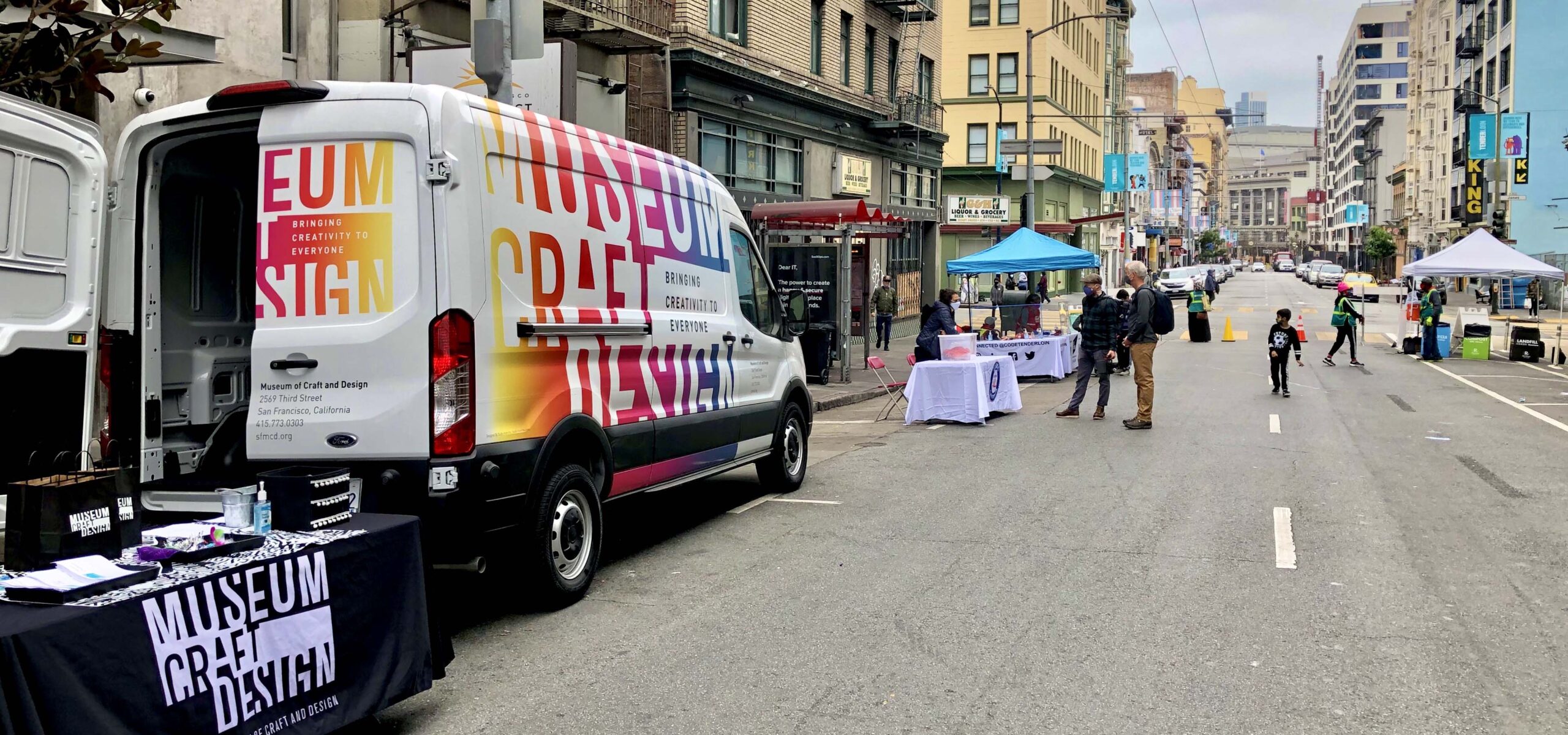 MakeArt van and table set up in street with people walking around