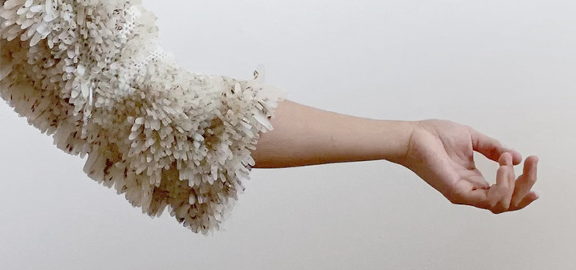 A person's arm, who is wearing a hydroponic garment that is sprouting seeds.