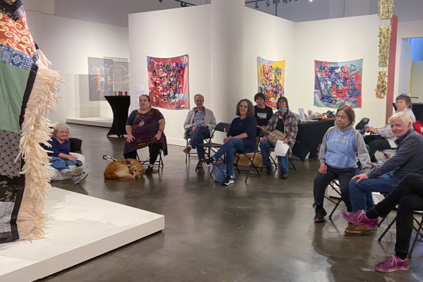 A group of peoplpe sit and listen to a description of an art piece during Access After Hours