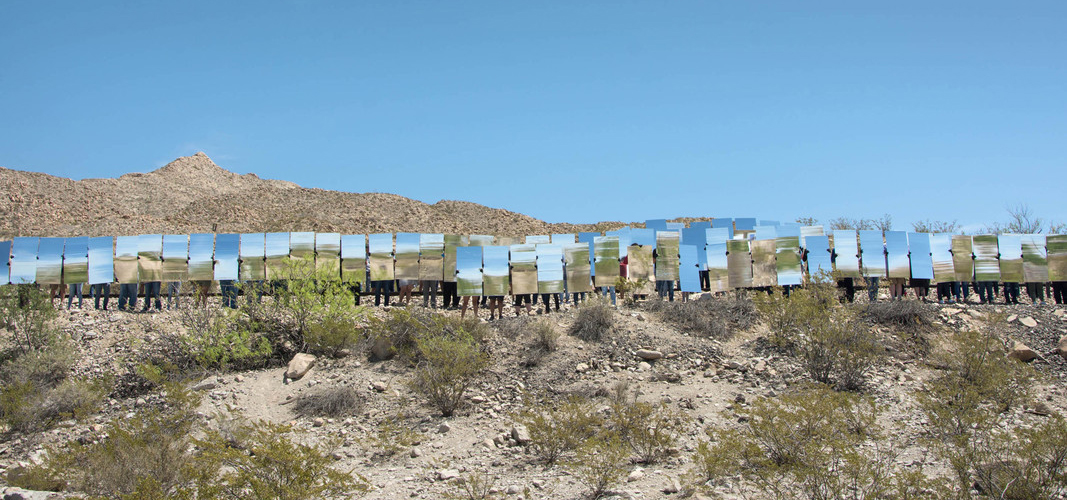 people in the desert holding up large scale mirrors.