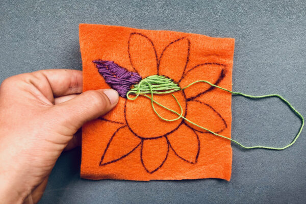 Embroidering a picture of a flower onto felt.