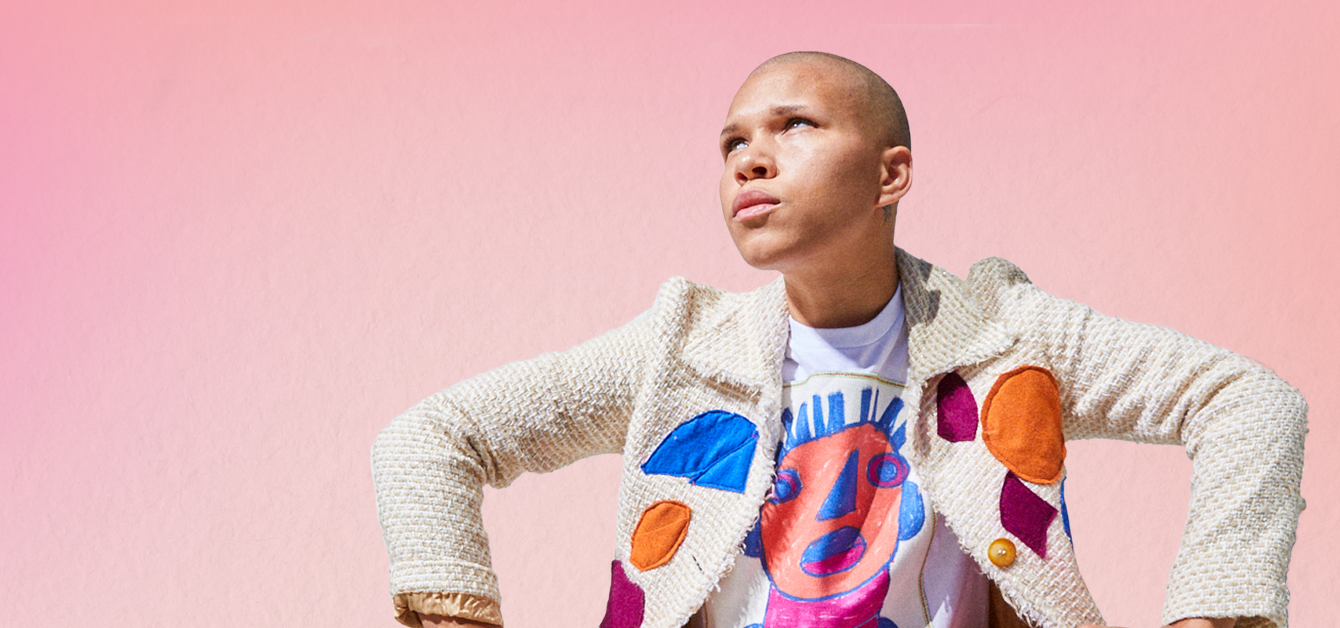 Model wearing embroidered jacket and designed shirt, posing on a pink background