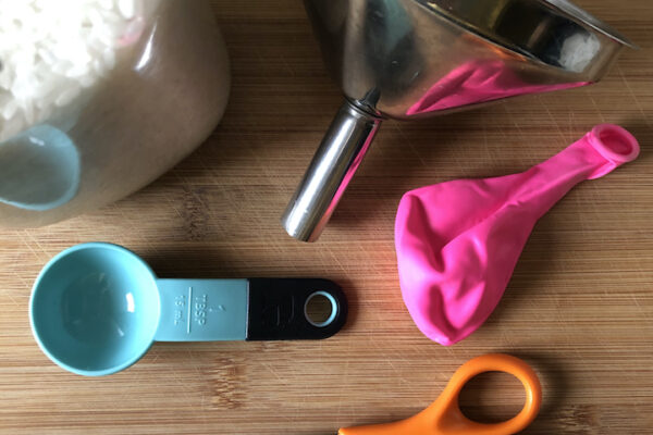 scissors, funnel, pink ballon, jar of rice and tablespoon on wooden table