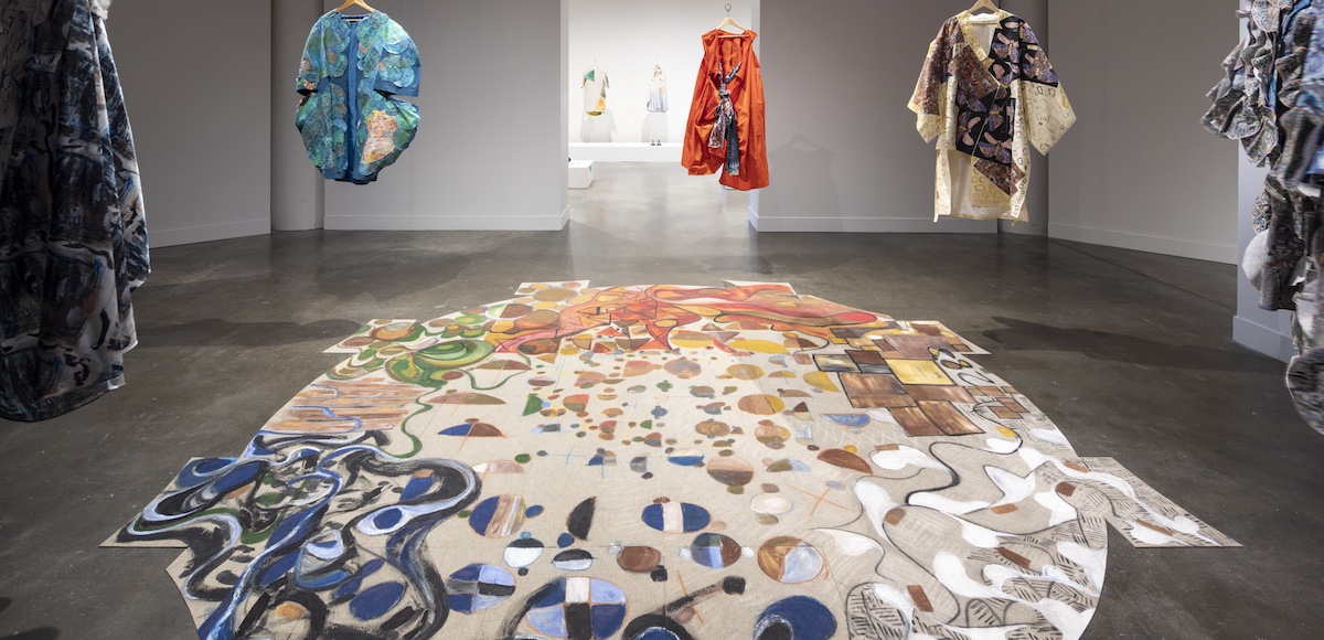 Handmade garments hung in a circle in open space with multi color rug underneath