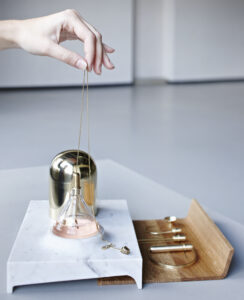 Perfume tools made of brass, marble, and glass sitting on oak tray on marble counter