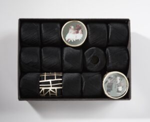 Five rows of black circular objects with three broaches in rectangle box
