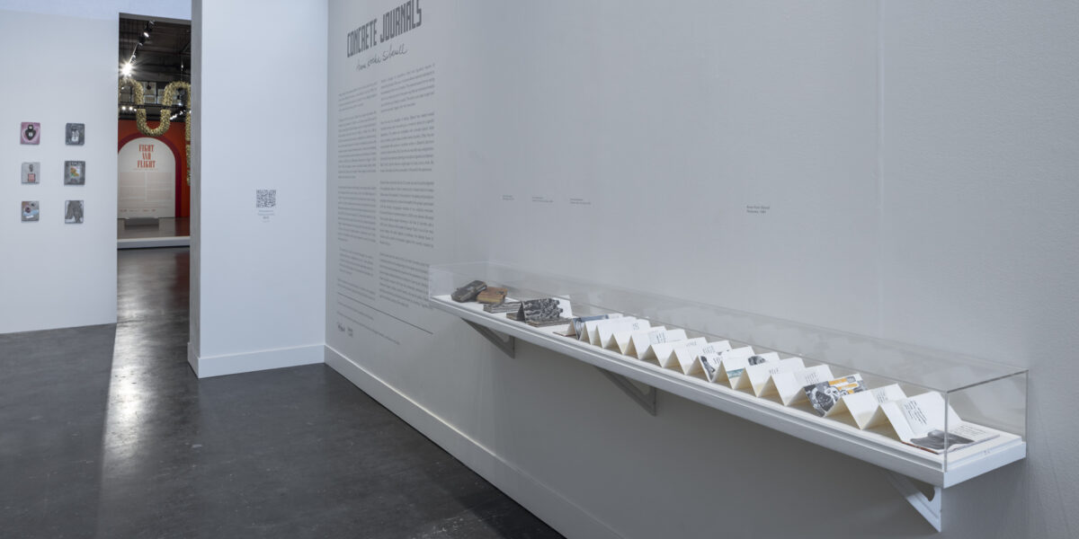 Exhibition photo of Concrete Journals: Anne Hicks Siberell. Items shown in a enclosed case on a shelf on the wall.