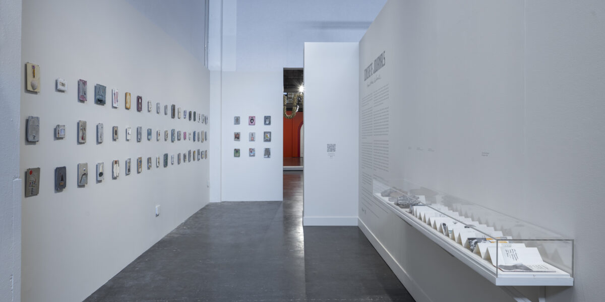 Exhibition photo of Concrete Journals: Anne Hicks Siberell. Items shown in a enclosed case on a shelf on the wall and hanging on a wall.