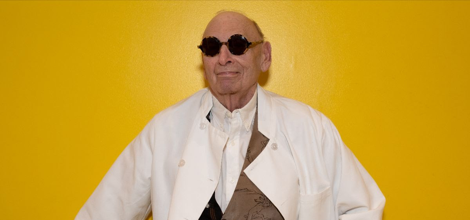 Ted Cohen standing in white jacket with sunglasses and yellow background