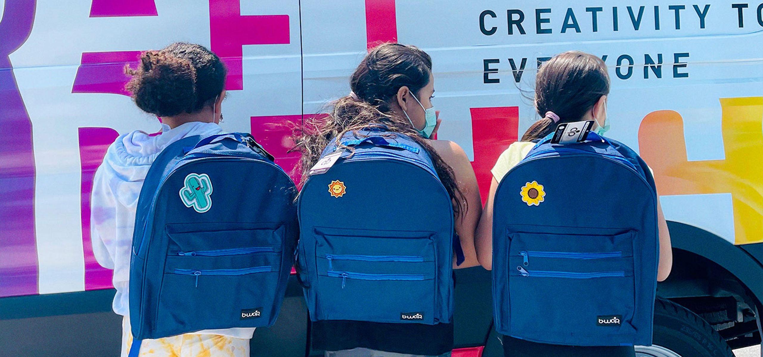 Three children showing off their backpacks in front of the Mobile MakeArt van