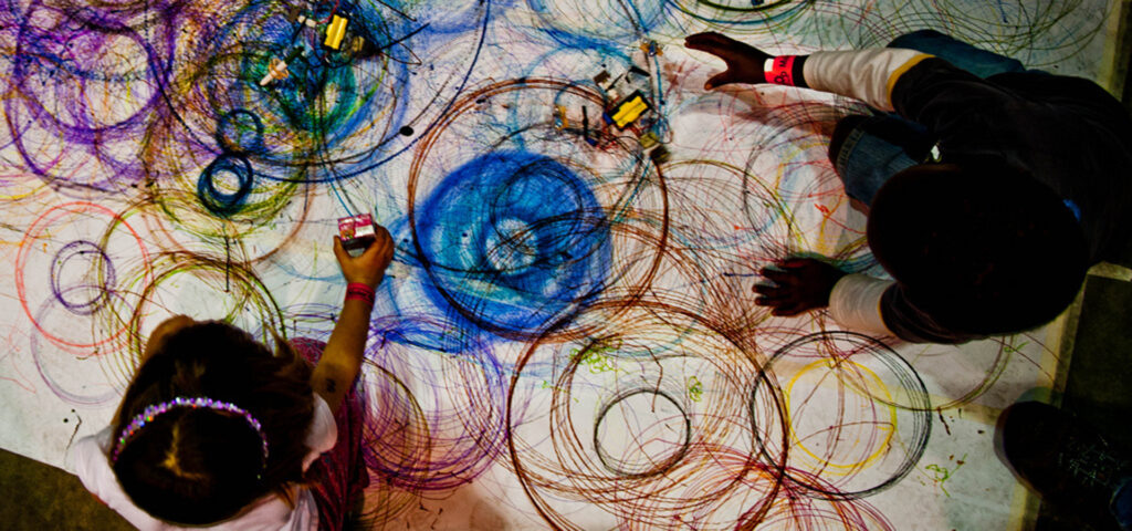 View from above of Spinning artbots and two people drawing with them, creating colorful circles