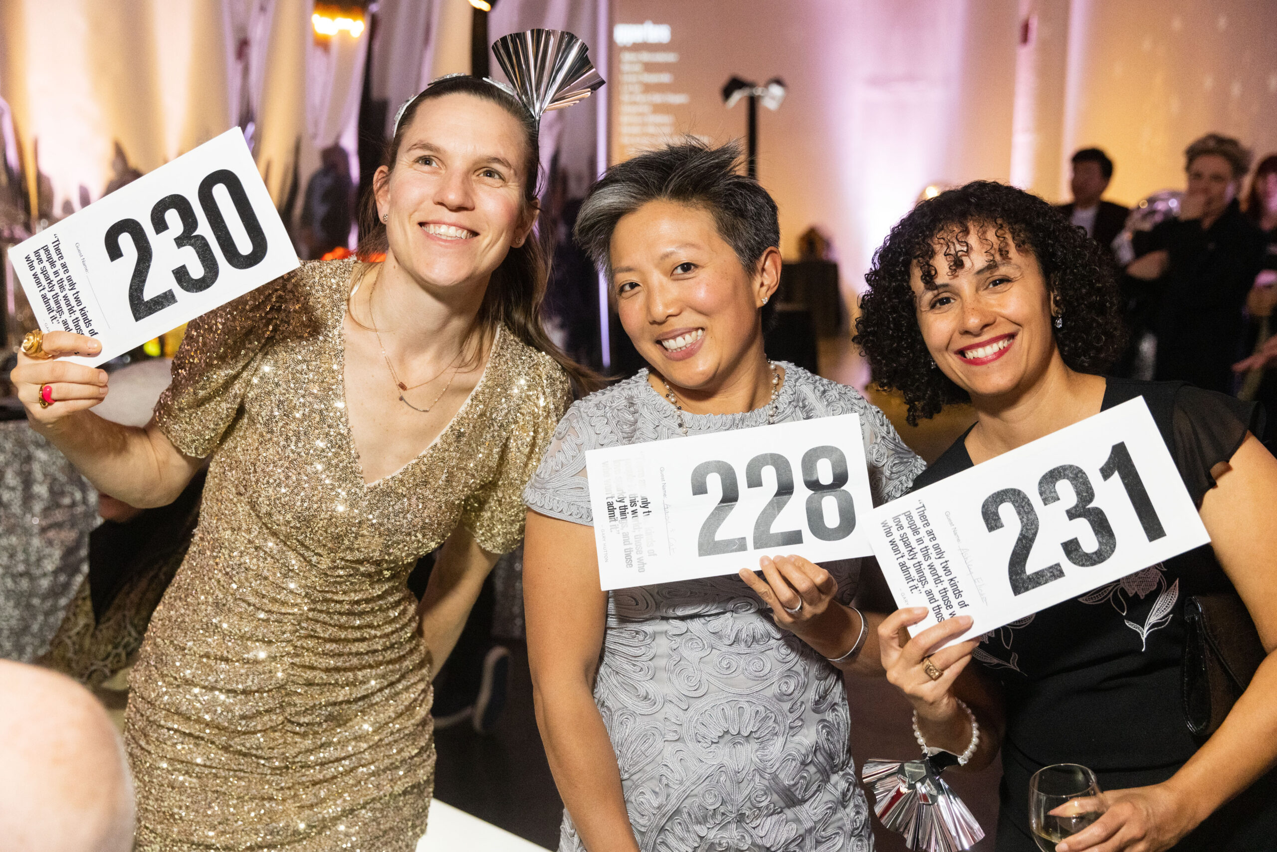 Three ladies holding up black and white auction bid numbers.