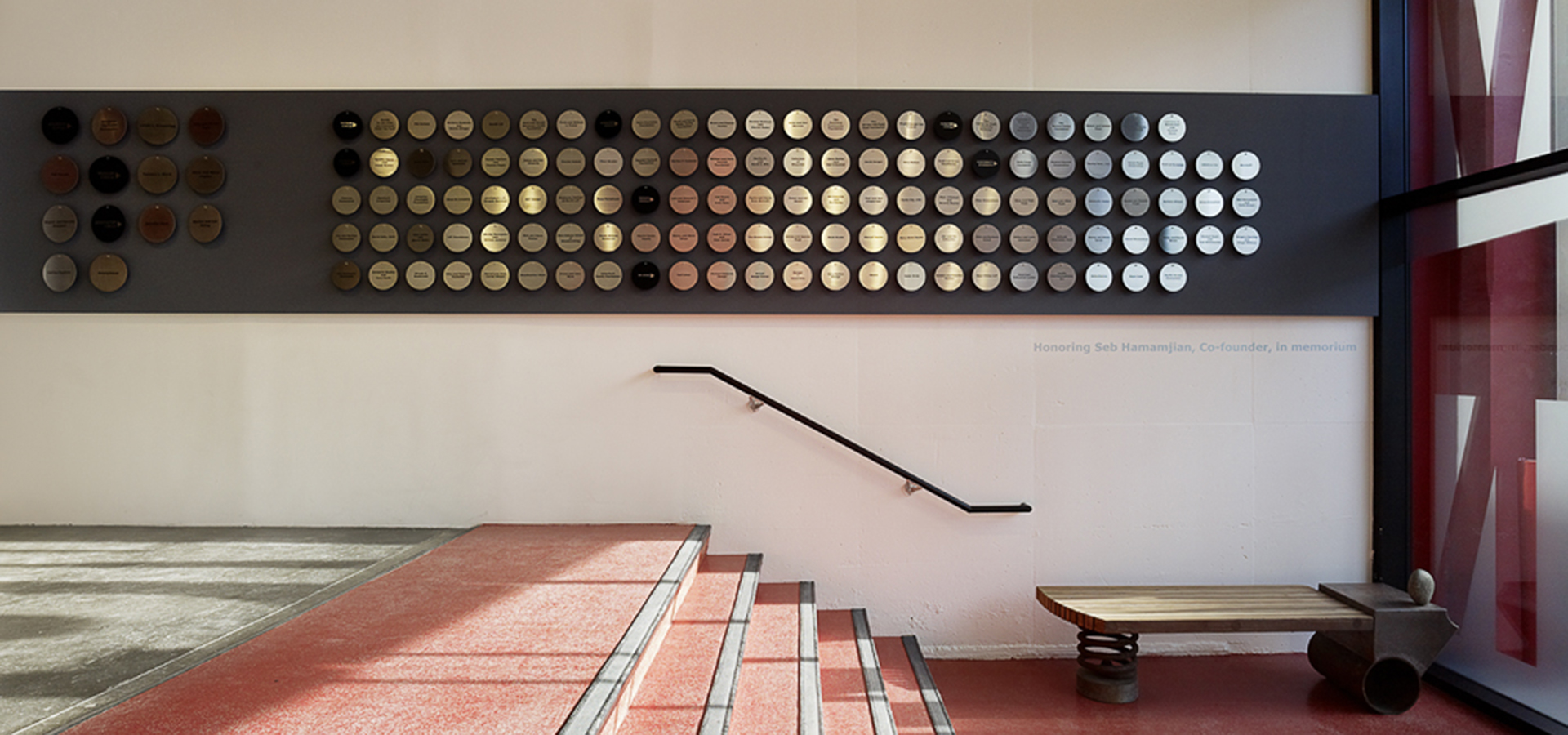 Photo of donor wall metal discs along a grey stripe on the wall with four red steps in front of it.