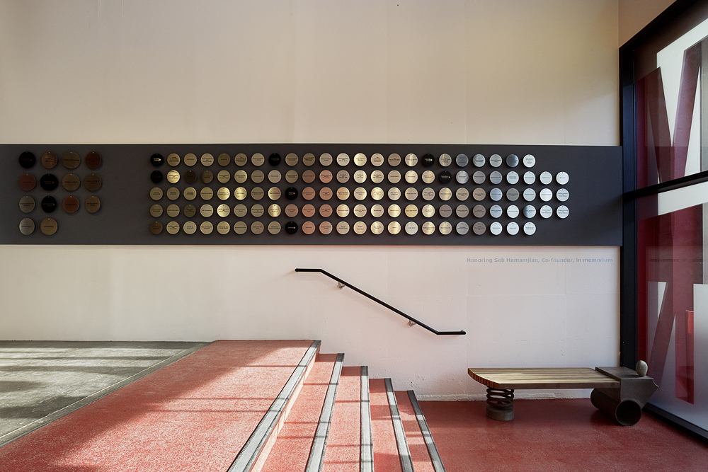 Photo of donor wall metal discs along a grey stripe on the wall with four red steps in front of it.