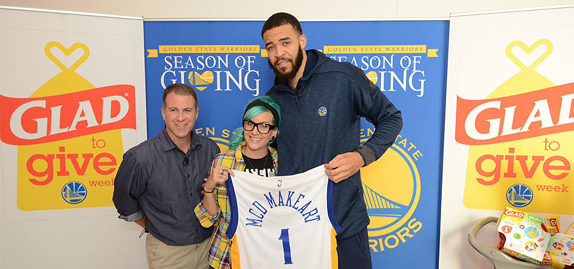 Image of three people holding of golden states warrior jersey that says MCD Makeart