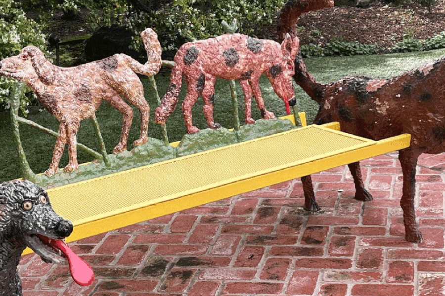 Photo of four ceramic sculptures of dogs around a yellow bench on herringbone brick patio