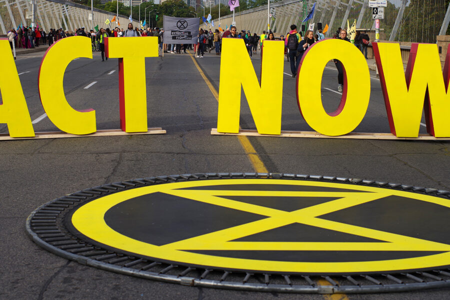 Photo of large yellow letters spelling out ACT NOW on a street with people in the distance behind it