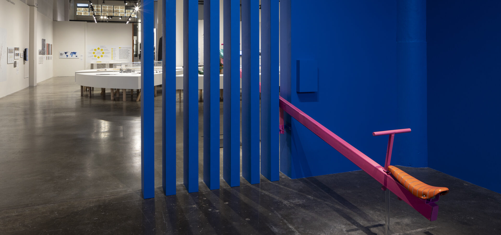 Artwork installation at the Museum of Craft and Design. Half of a pink teeter-totter coming out of a blue slatted wall.