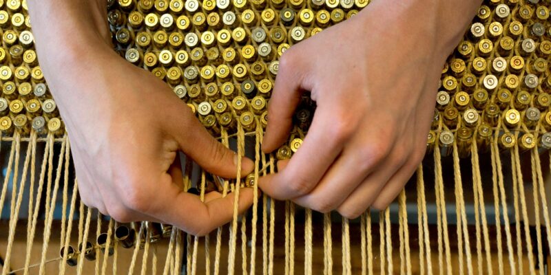 Photo of hands weaving gold bullets and string.