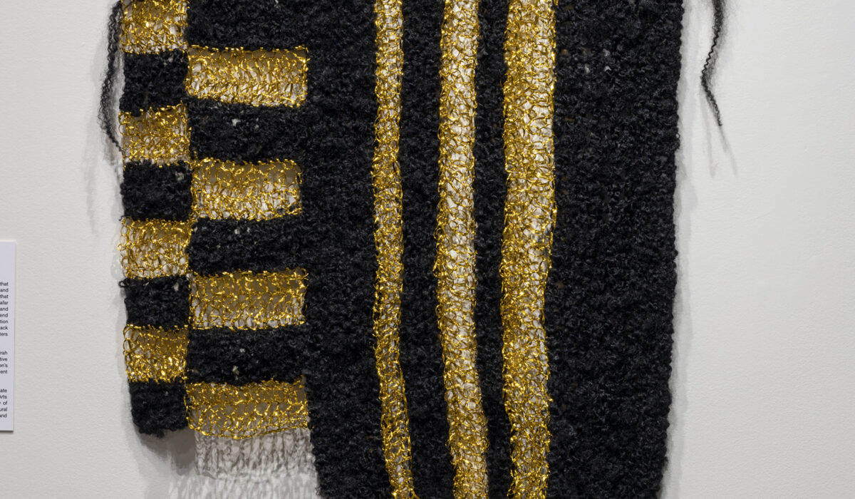 Artwork hanging on a wall. Black and gold textile to form vertical pattern.