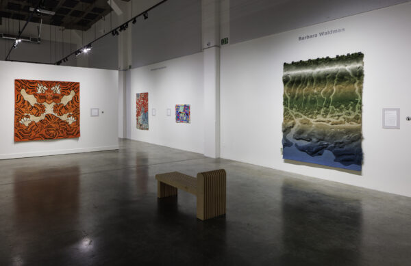 Photo inside a museum of an exhibition featuring rugs hanging on walls and on pedestals on the floor.