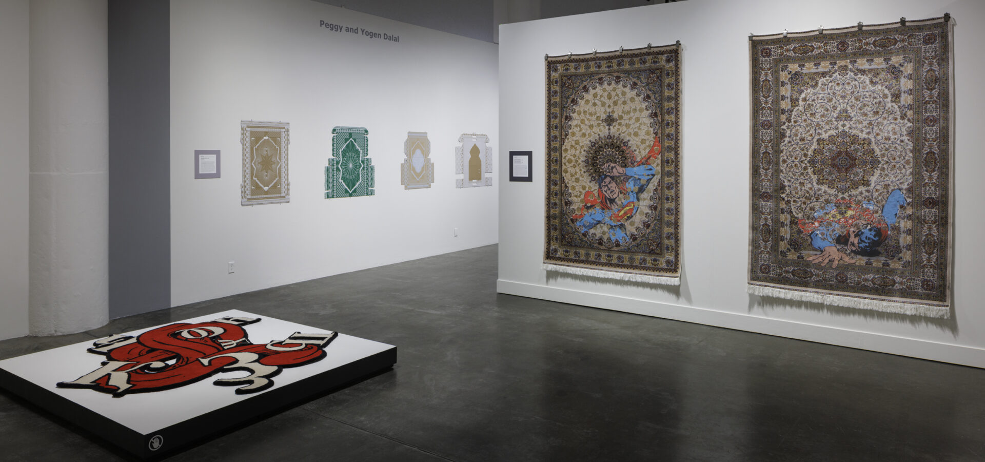 Photo inside a museum of an exhibition featuring rugs hanging on walls and on pedestals on the floor.