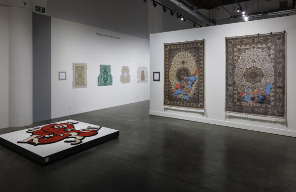 Photo inside a museum of an exhibition featuring rugs hanging on walls and on pedestals on the floor.