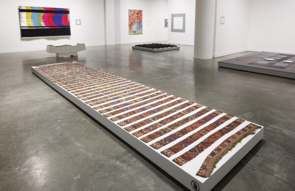 Photo inside a museum of an exhibition featuring rugs hanging on walls and on pedestals on the floor.