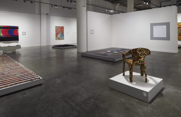 Photo inside a museum of an exhibition featuring rugs hanging on walls and on pedestals on the floor.