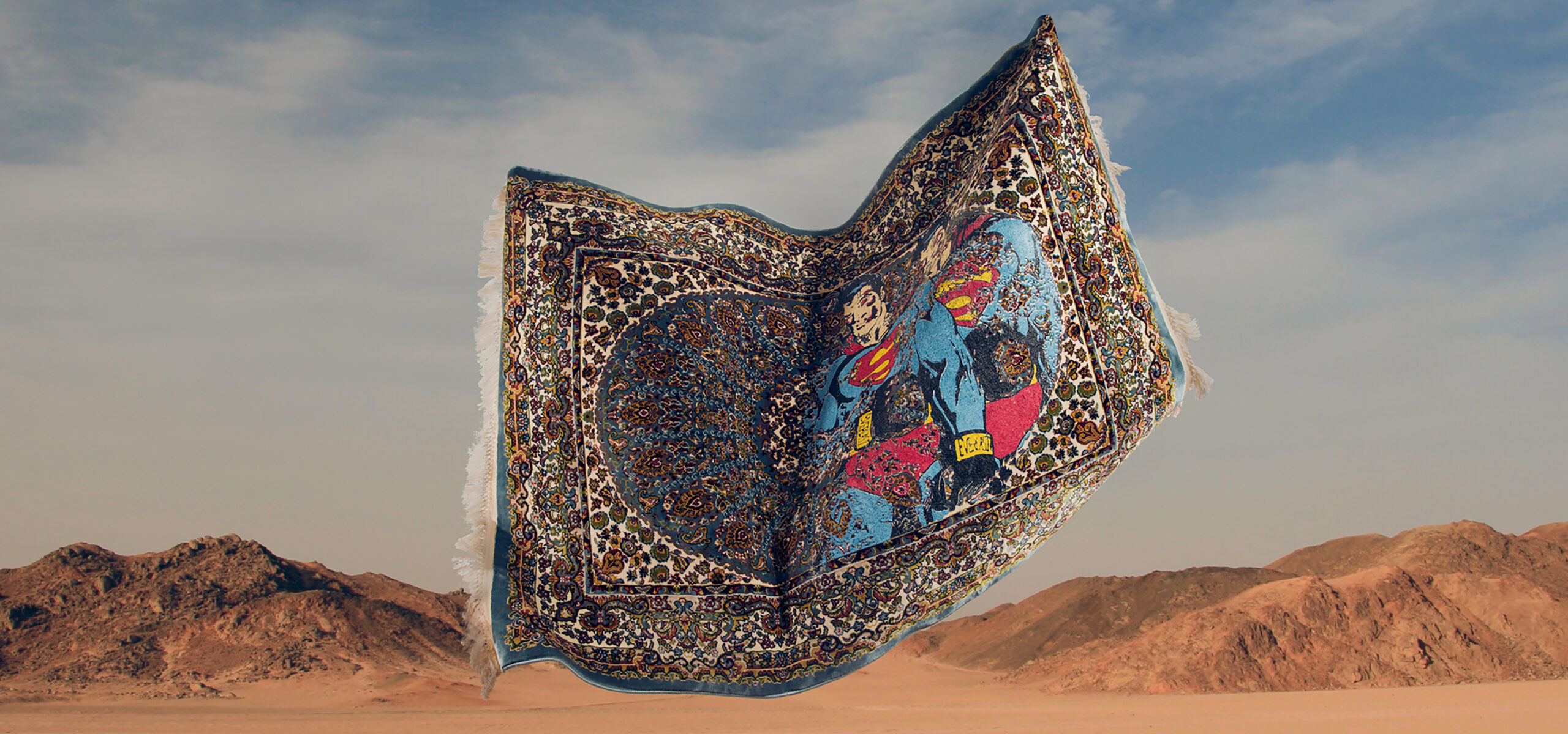 Picture of a rug flying in the air with sand and mountains behind it