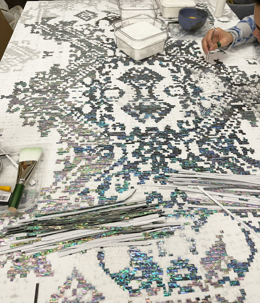 Photo of artist's hand working on placing bead dots on a artwork