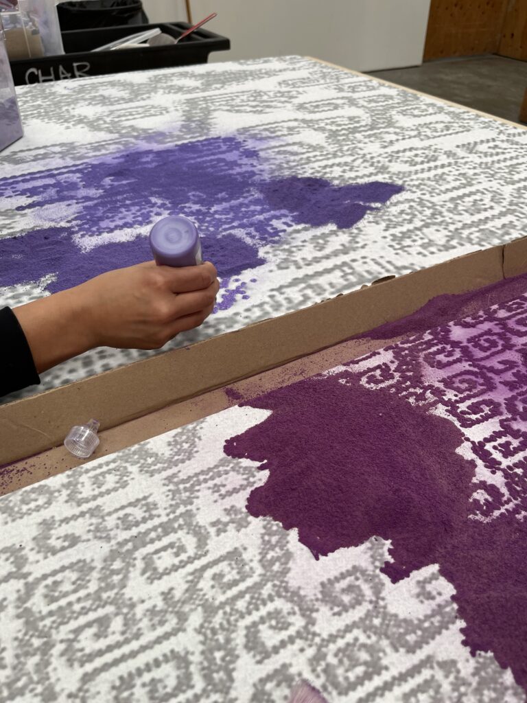 photo of artist placing purple powder over small dots to make up a larger artwork pattern