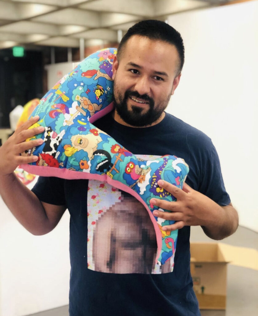 Photo of Alexander Hernandez holding one of his plush artworks over his shoulder.