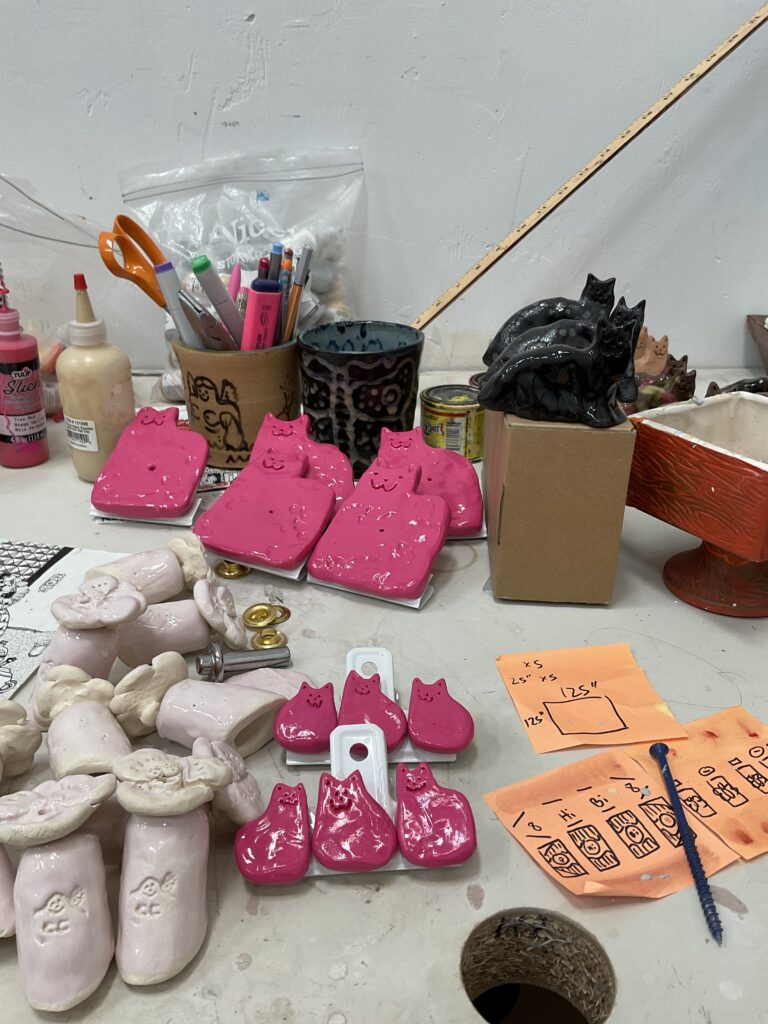 Photo of artist table with supplies and pink ceramic cats