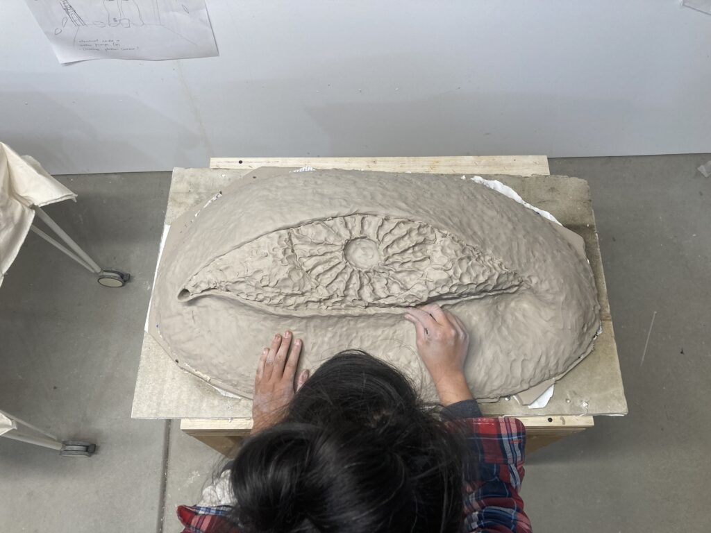 larger round ceramic artwork of an eye with person sitting working on it.