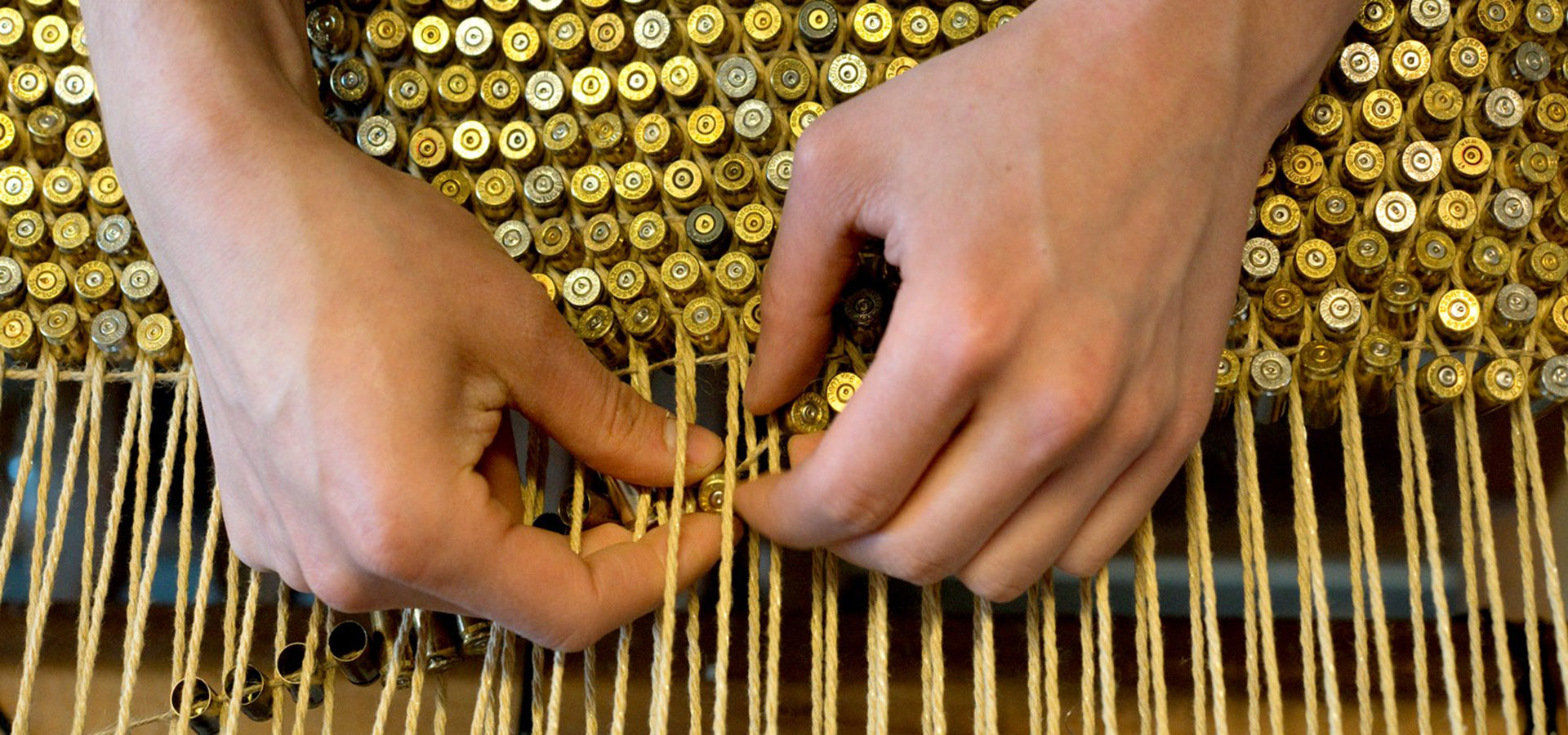 photo of hands weaving gold bullets on string into a rug
