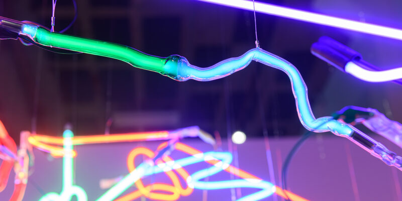 Close up photo of different colors of neon pieces suspended from the ceiling.