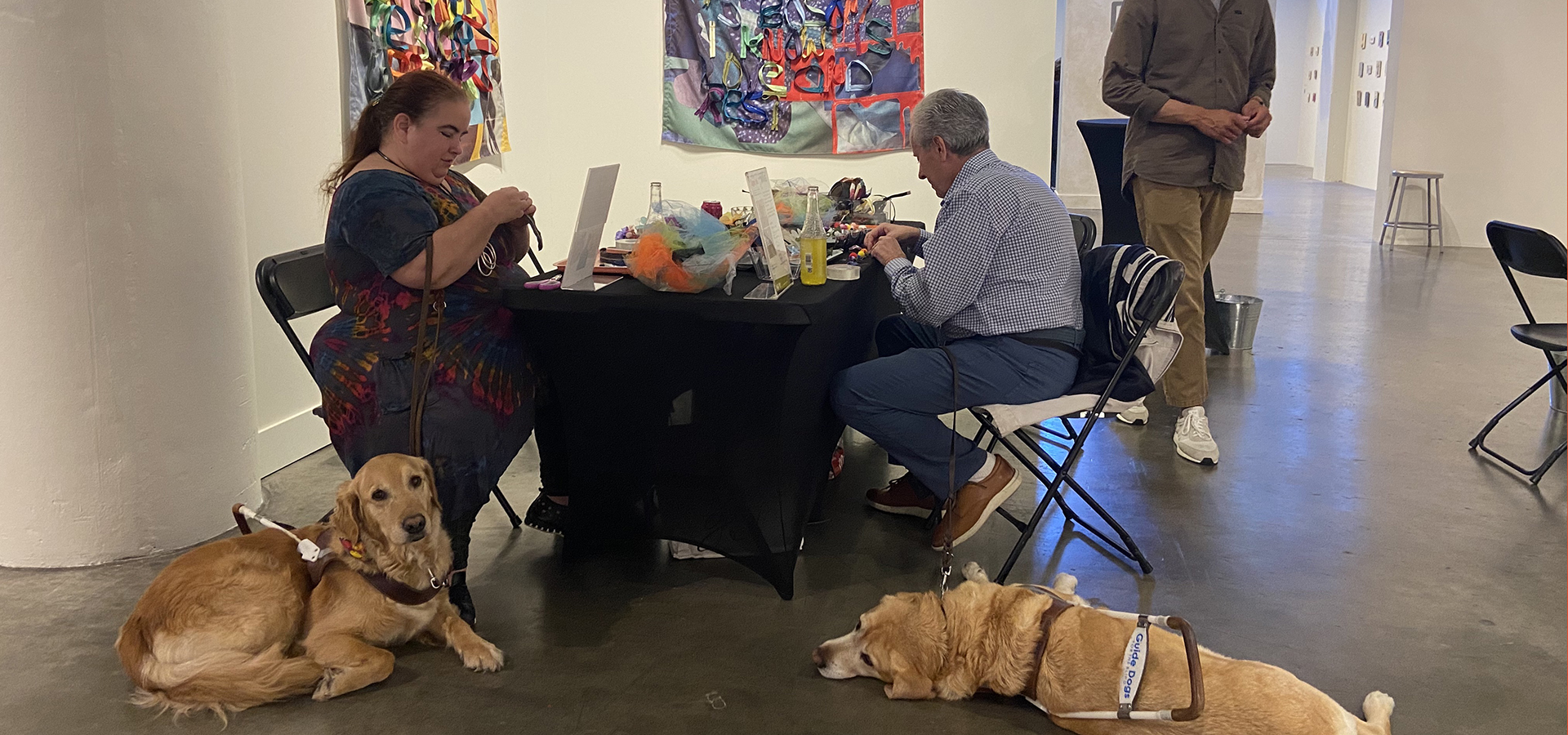 Photo of people sitting at a table crafting and two service dogs sitting near their chairs