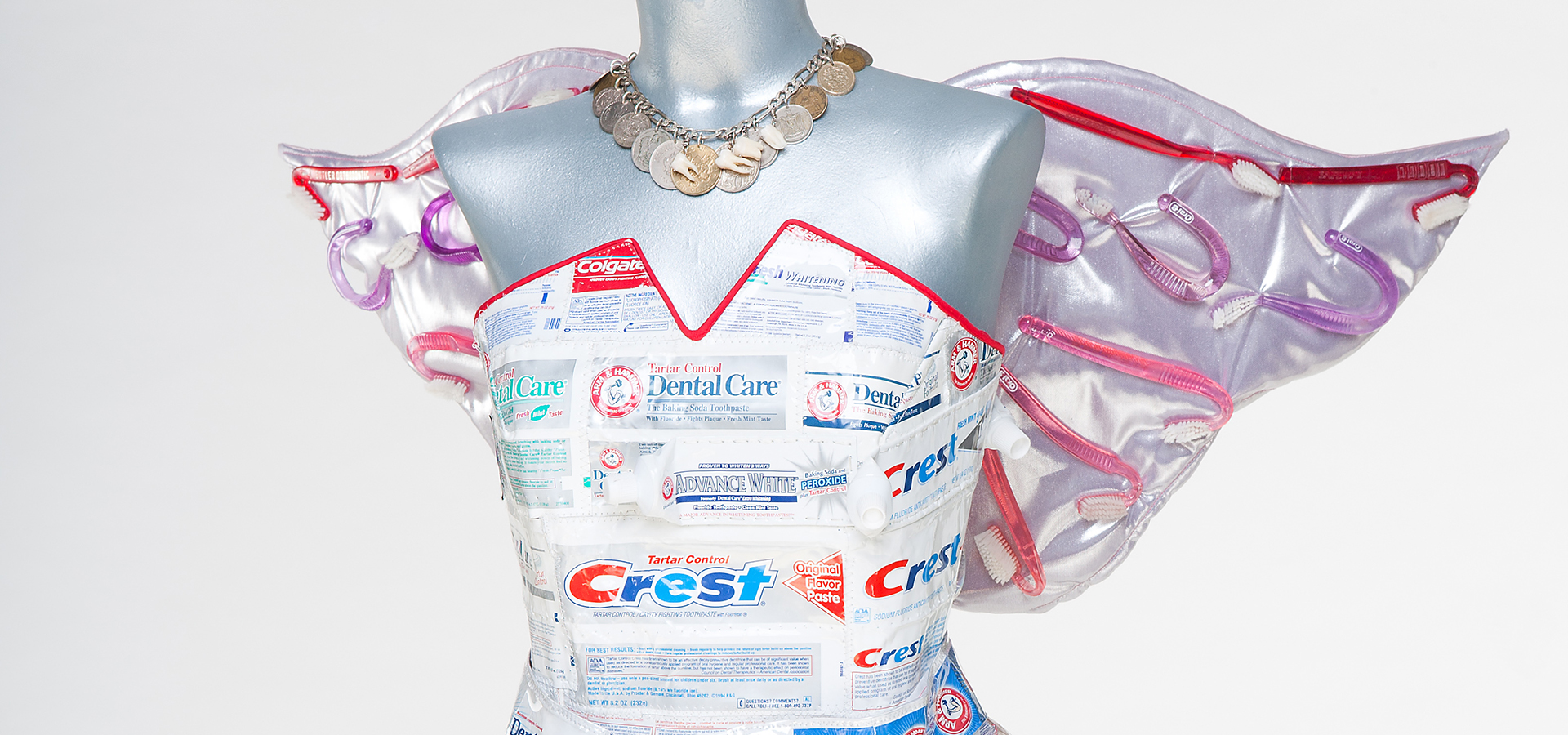 Photo of a dress with wings on a mannequin made out of toothpast wrappers and dental cleaning materials.