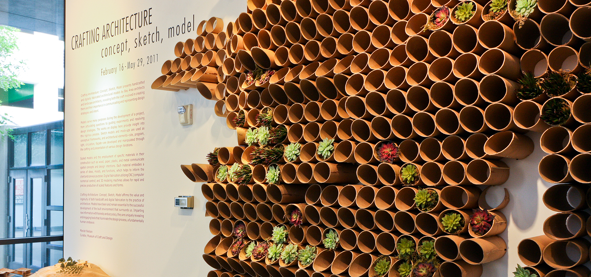 Photo of an exhibition marque wall with lots of small wooden circles coming out o f the wall holding plants.