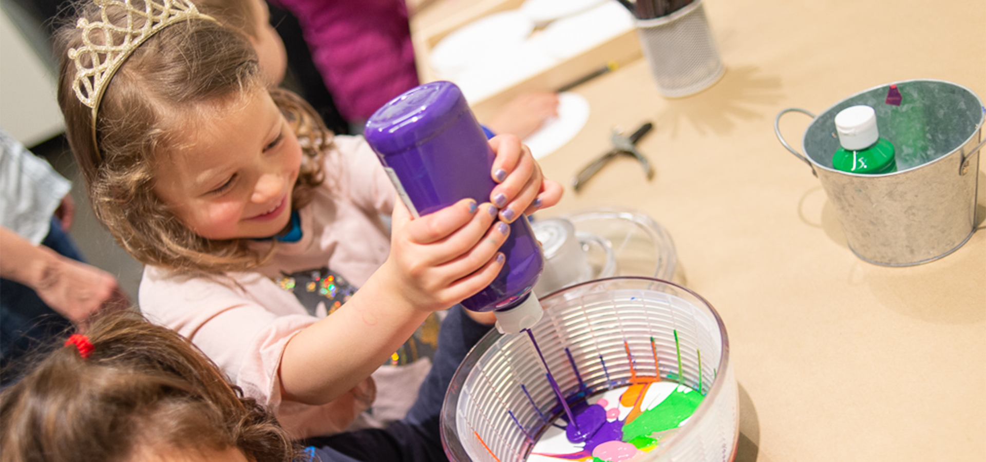 A young child squeezes a bottle of purple paint into a bowl