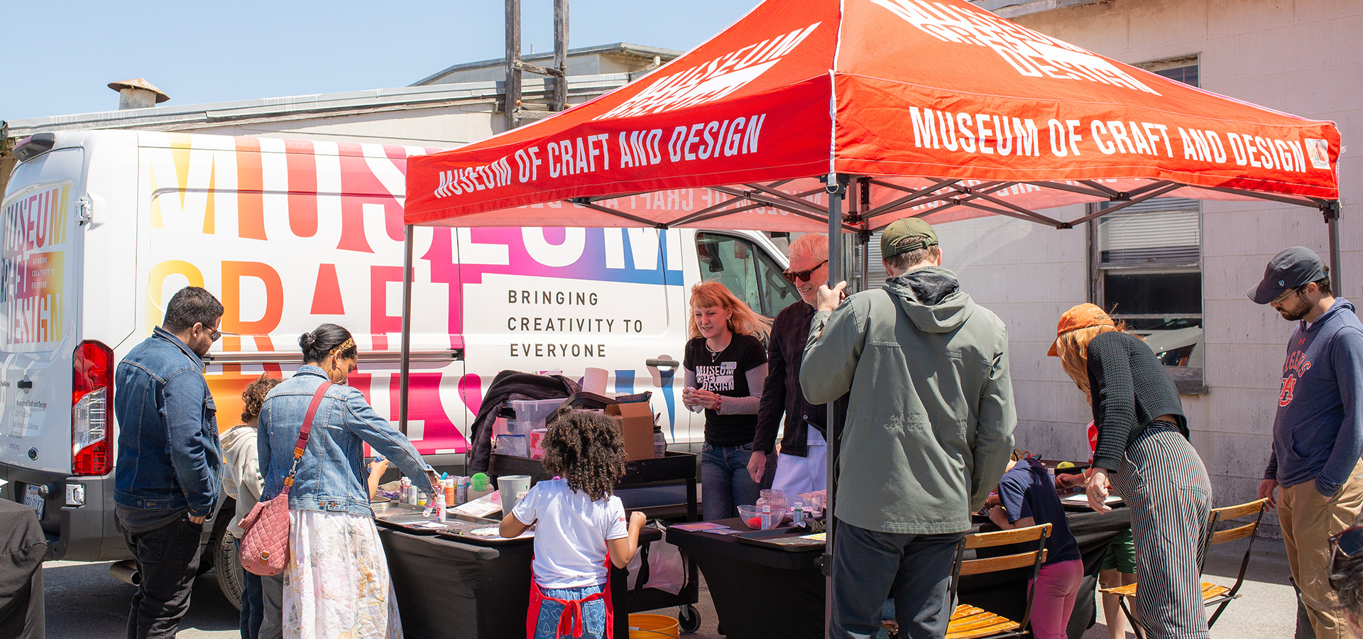 Photograph of people standing around and engaging with a mobile MakeArt activation in an outdoor location